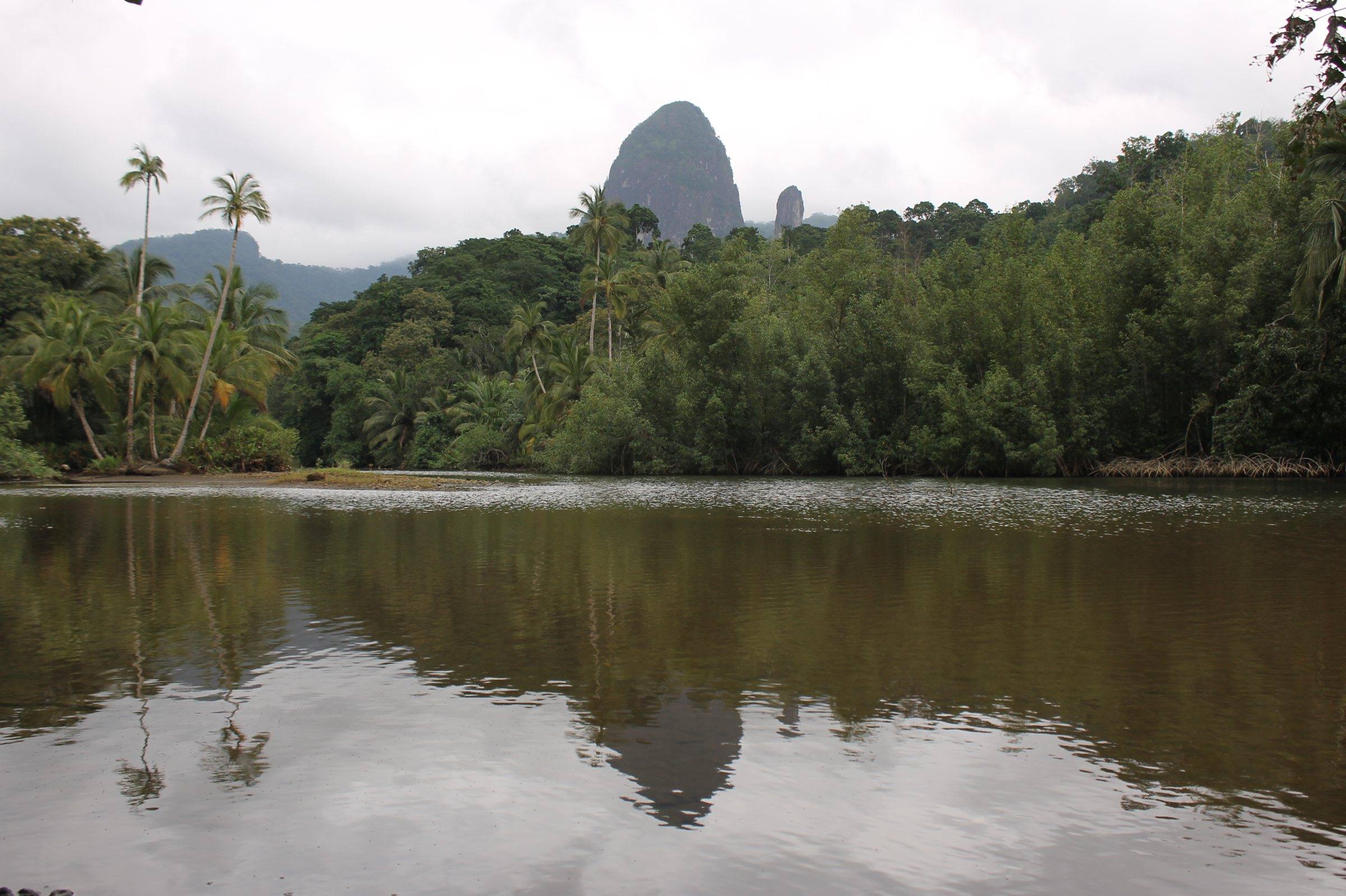 Volcanic spires above palms and a still lagoon at Praia Caixão