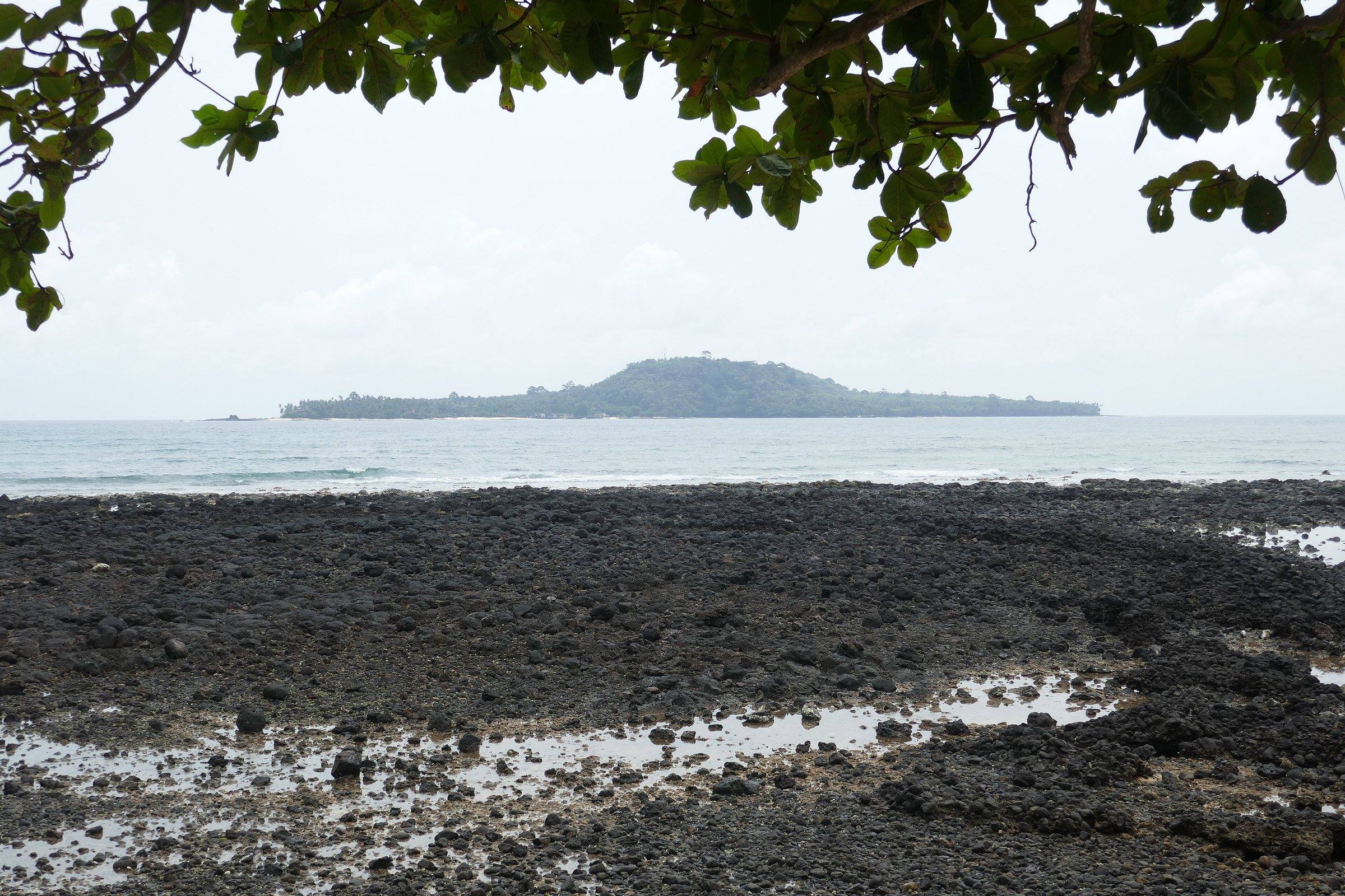 Ilhéu das Rolas seen across black volcanic rocks from Porto Alegre