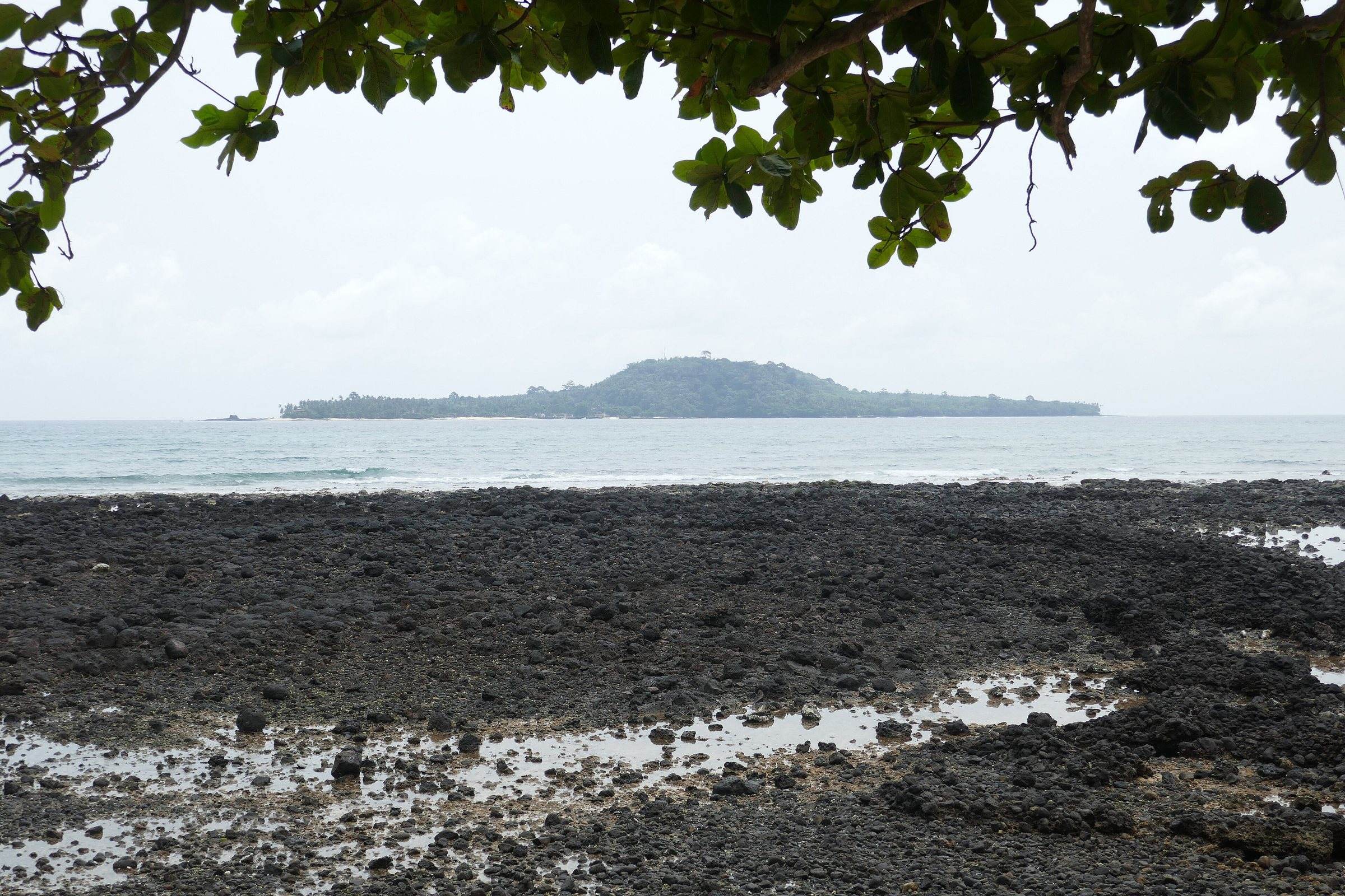 Ilhéu das Rolas seen across black volcanic rocks from the shore at Porto Alegre